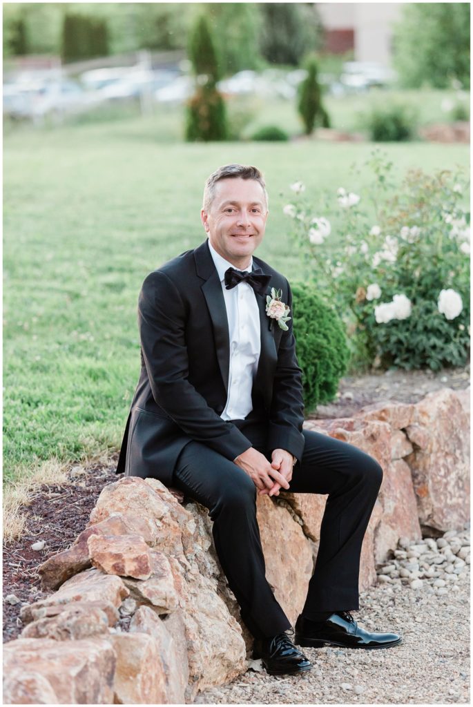 groom sitting on rock during outdoor bridals on wedding day