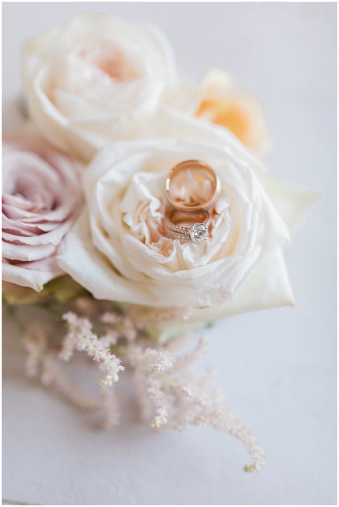 bridal bouquet with white and light pink roses and wedding rings in middle of flowers 