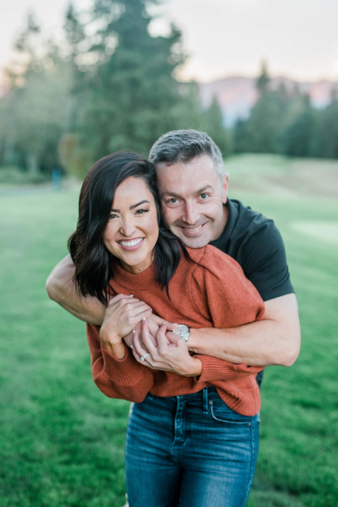 newly engaged couple hugging wearing orange shirt and black shirt at outdoor golf course engagement session