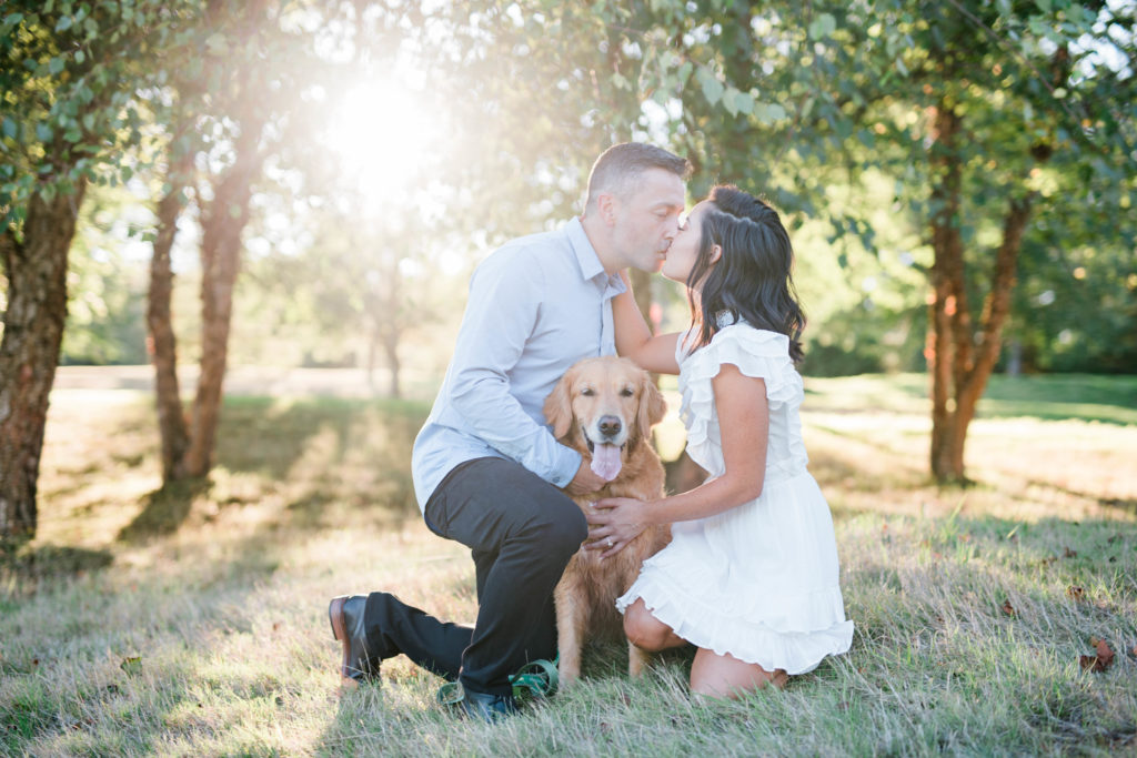 engaged couple kissing in golf course engagement session with beautiful golden retriever puppy