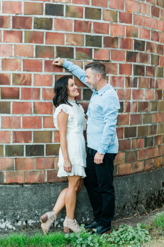 engaged couple talking and leaning against brick wall