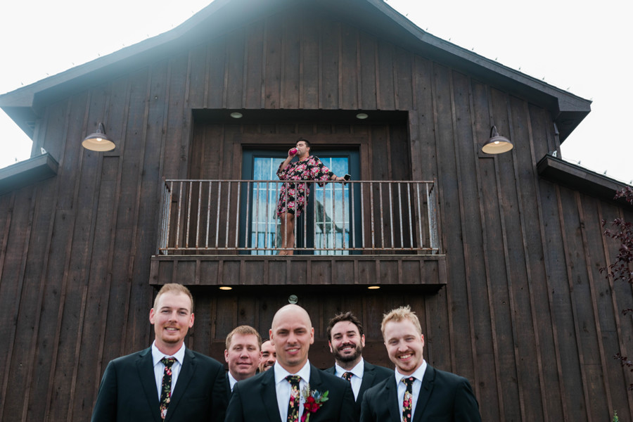 groomsmen posing for photos while bridesman surprises and poses on balcony