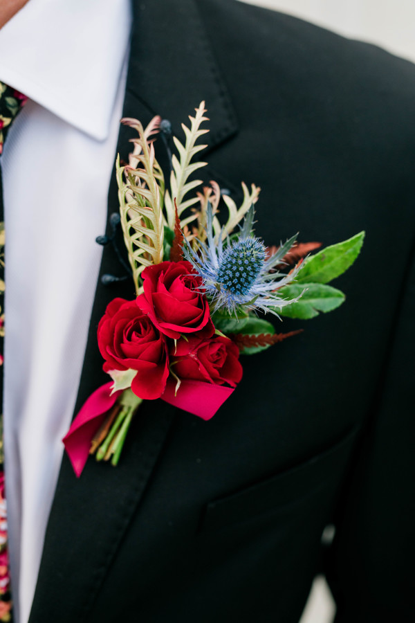 close up of groom's boutonnière with greenery, roses, and blue florals