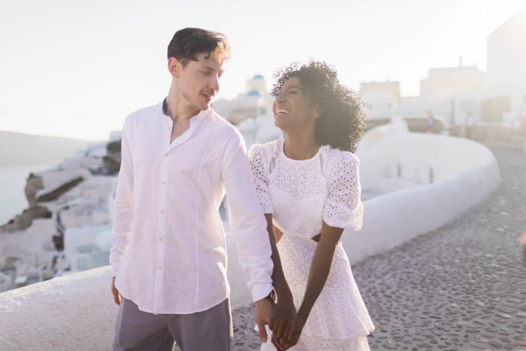 man and woman holding hands and walking together through Santorini for their destination engagement session