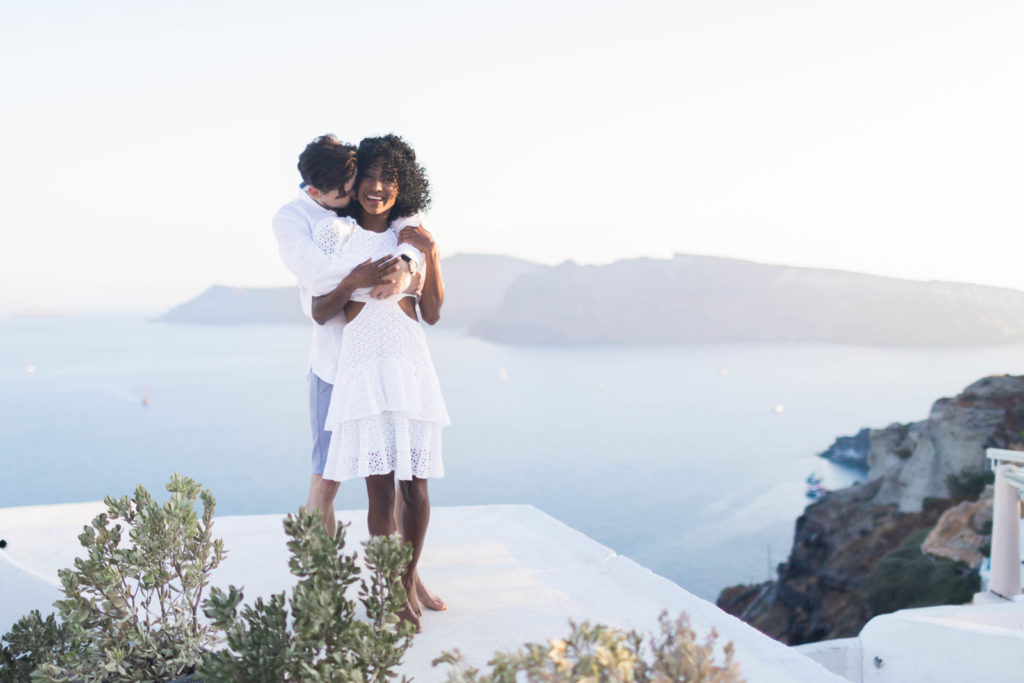 destination engagement photos with man embracing woman from behind her with the ocean behind them 