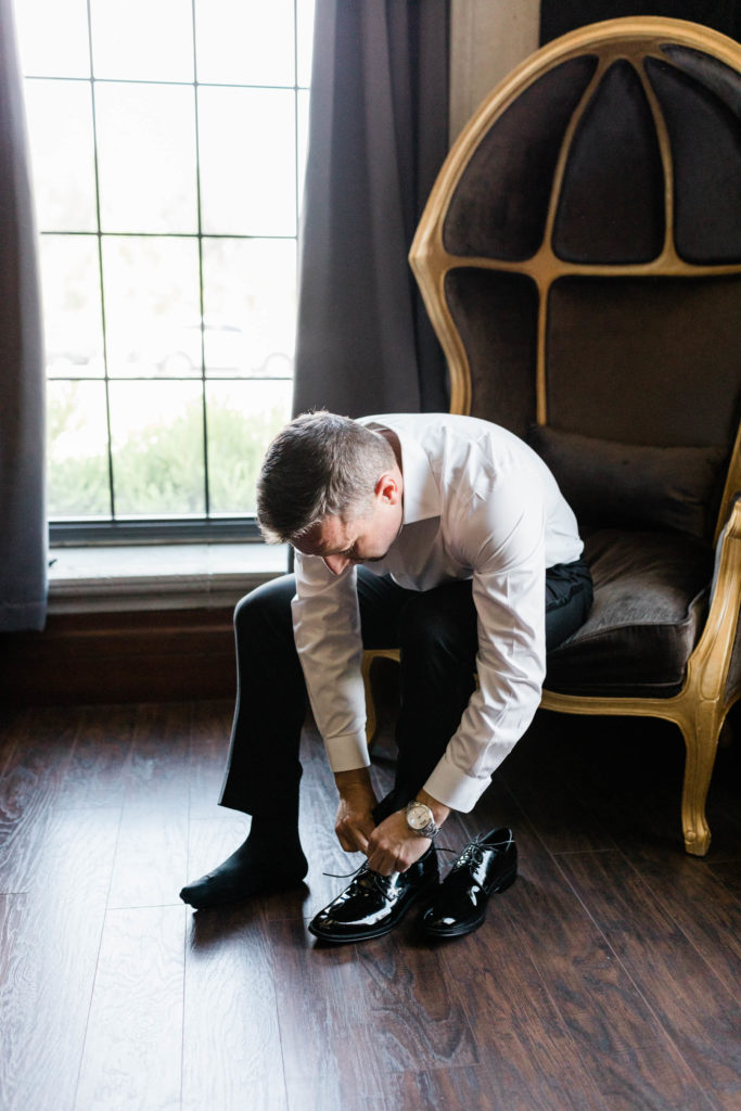 groom fixing his shoes as he sits on a wicker chair at his Boise wedding venue