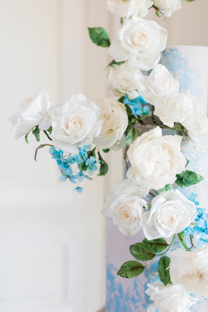blue and white floral arrangement that is on the side of a wedding cake for a elegant wedding