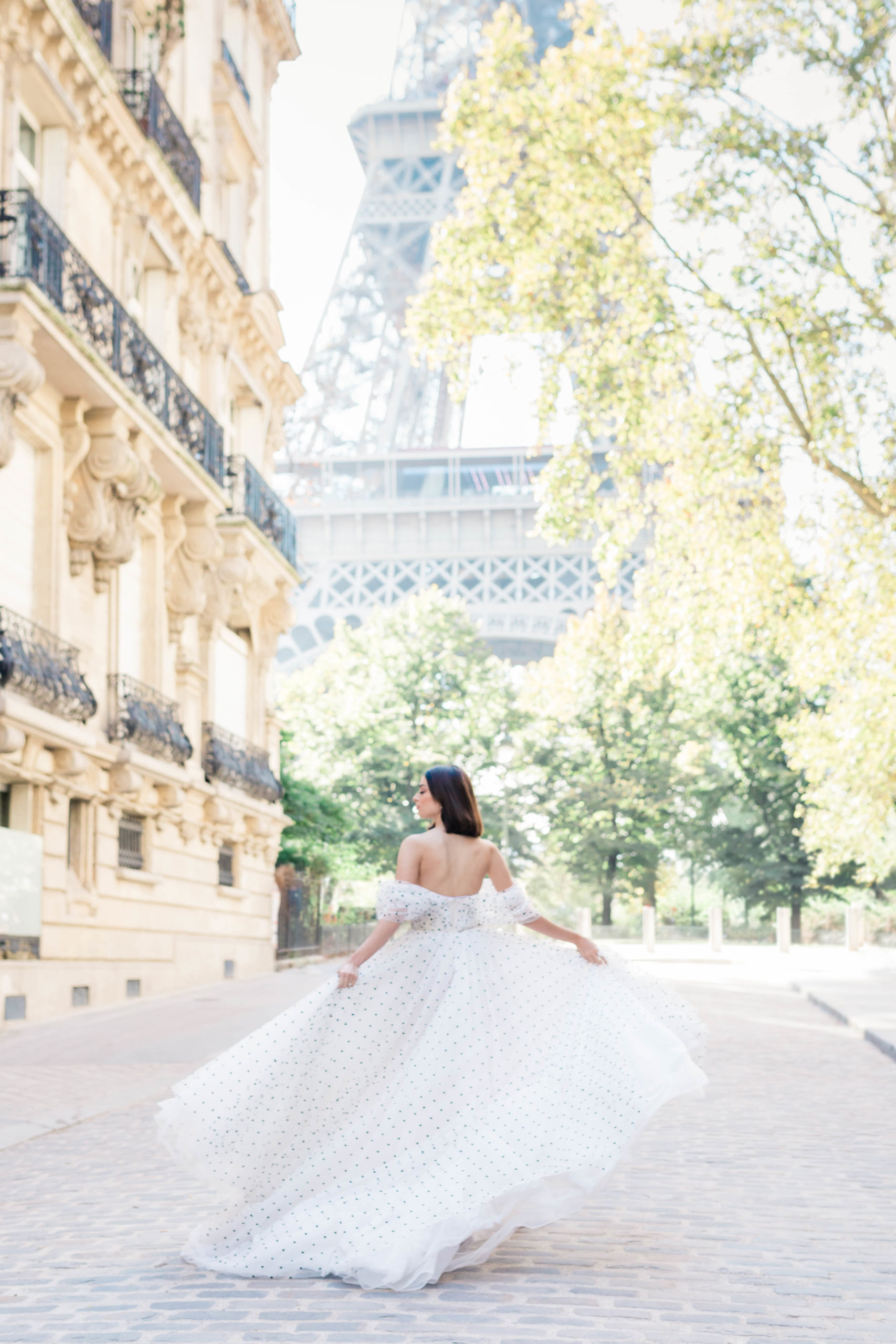 woman in a white dress dances in the streets of Paris France for her engagement photos