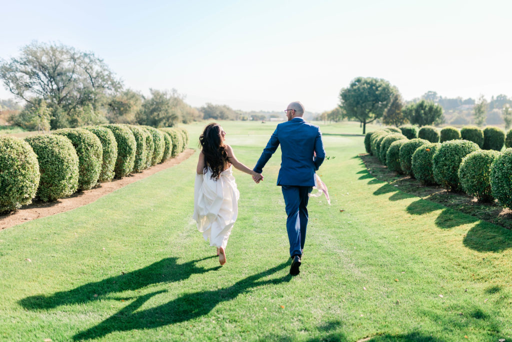bride and groom holding hands and running away from the camera towards an open field