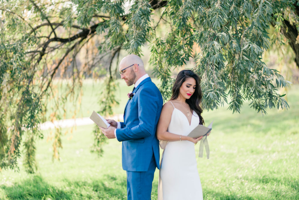 bride and groom standing back to back while reading their vows at their outdoor wedding venue