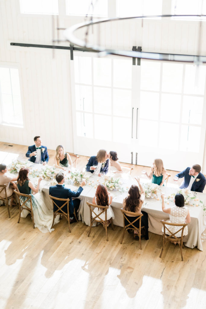 bride and groom kissing at a reception table surorunded by their friends and family in Boise Idaho wedding venue 
