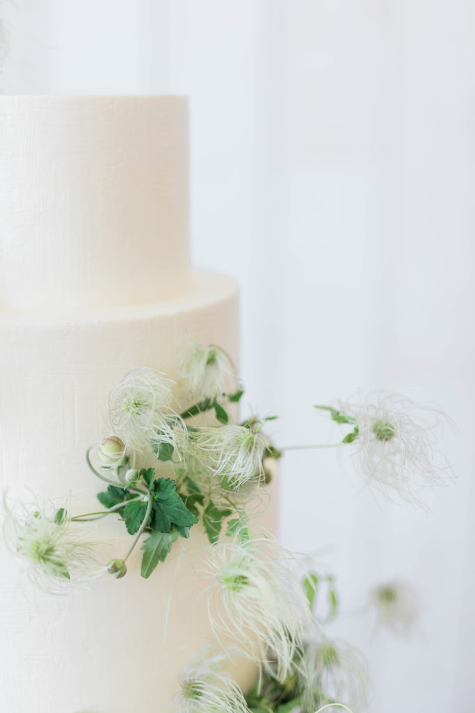 detail shot of white buttercream wedding cake with small greenery on the side
