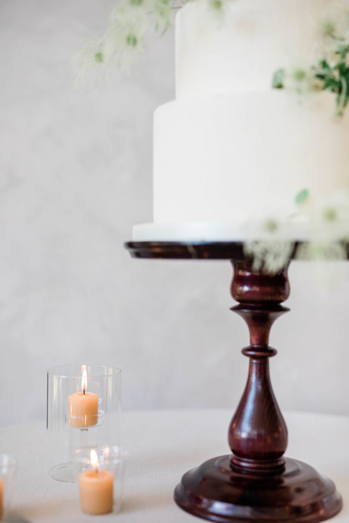 timeless wedding cake on a wooden cake stand and small tea light candles surrounding the stand