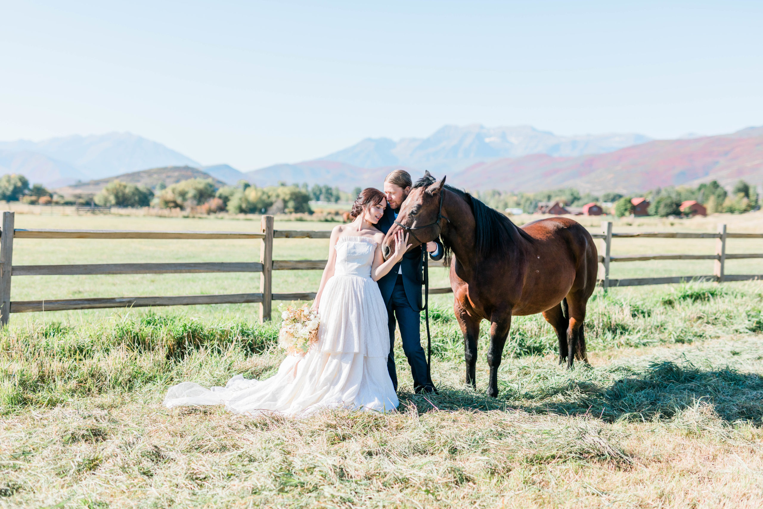Boise bride and groom posing in a field with a wood fence with a horse in Idaho