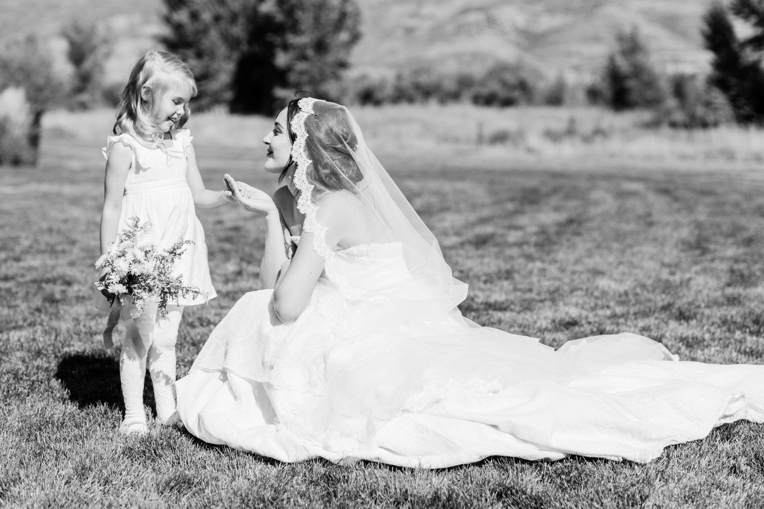bride and her flower girl sharing a special moment on the lawn on the wedding venue as the bride holds the flower girls hand and they smile at each other