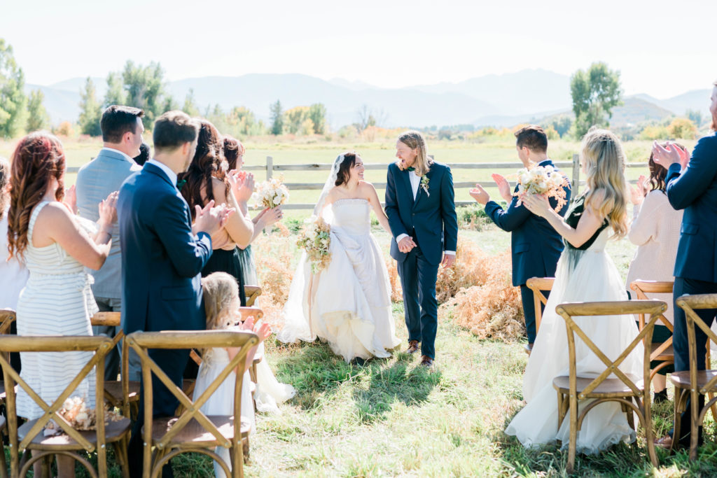 bride and groom walking down the aisle together for their outdoor wedding in Idaho with fields behind them and their friends surrounding them