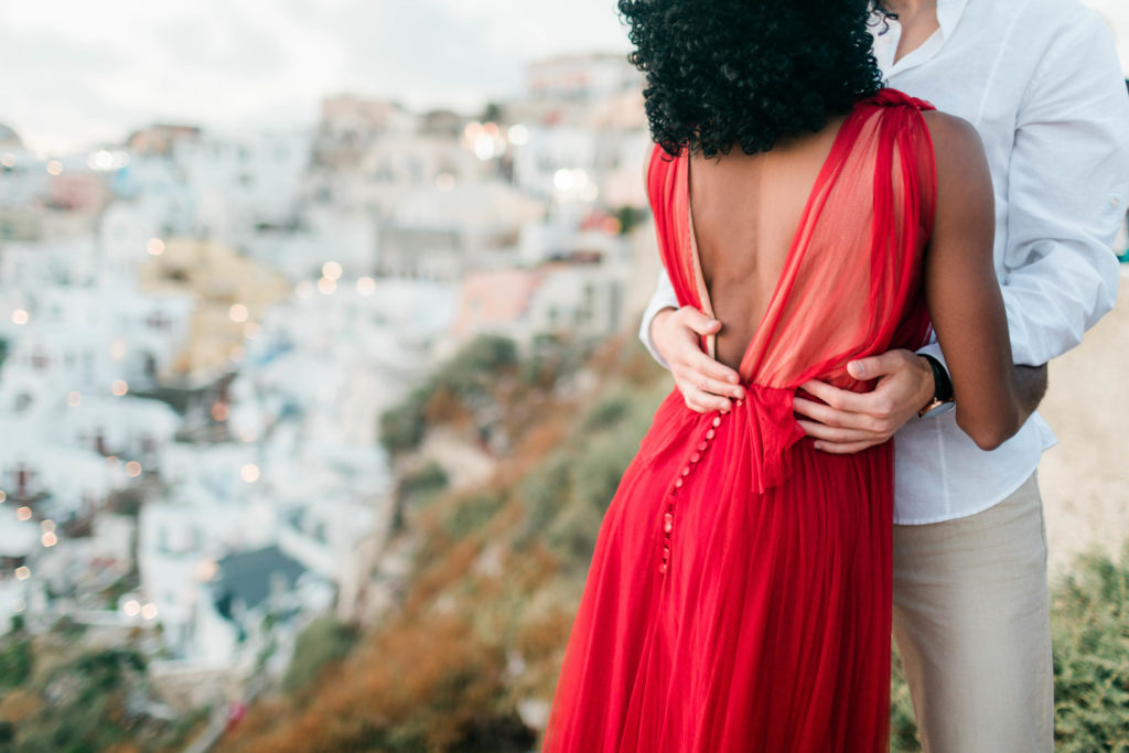 detail shot of man holding his fiances waist, woman in a red dress for their engagement photos with Greece's skyline behind them
