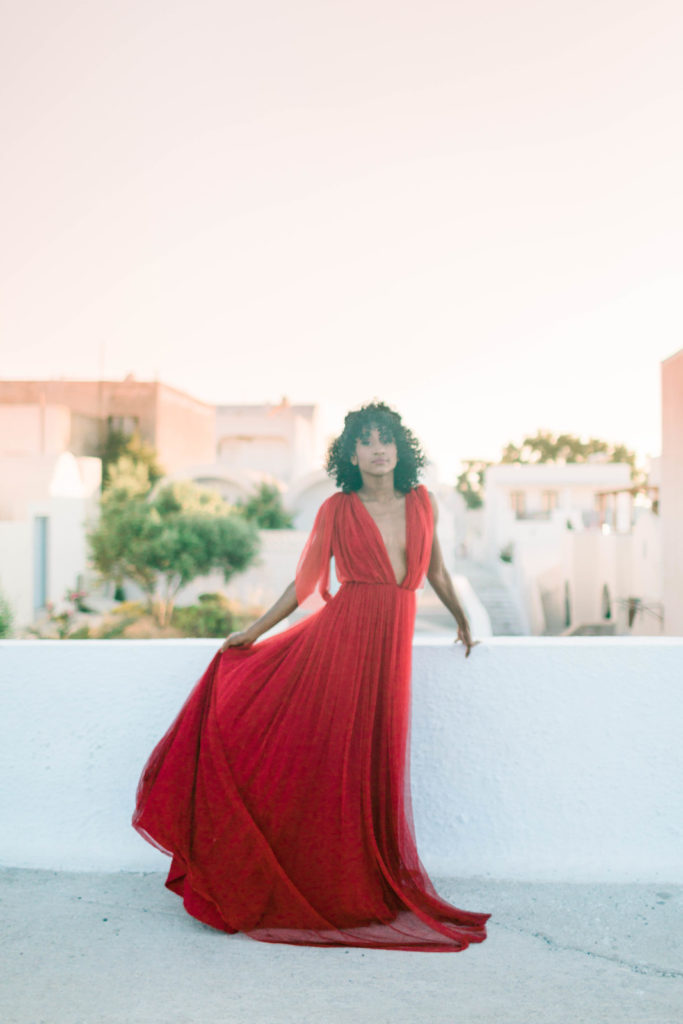 woman in a red dress posing for her engagement photos in Greece with the sun setting behind her