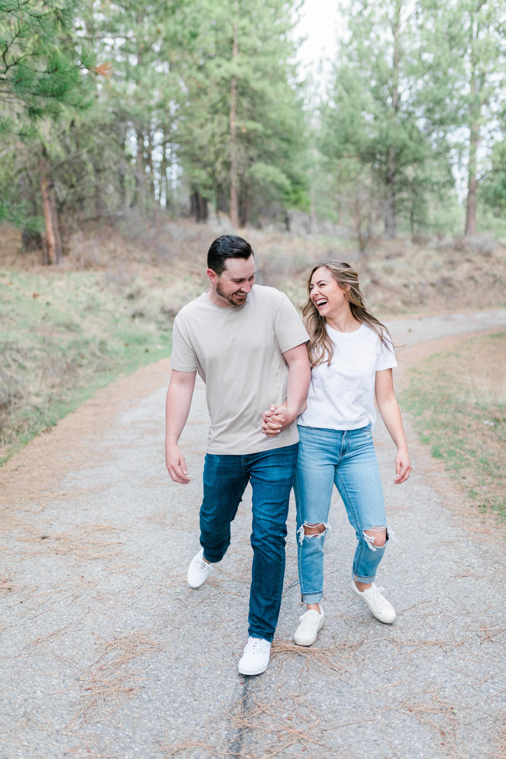 man and woman holding hands and walking down a dirt path as they bump their hips together
