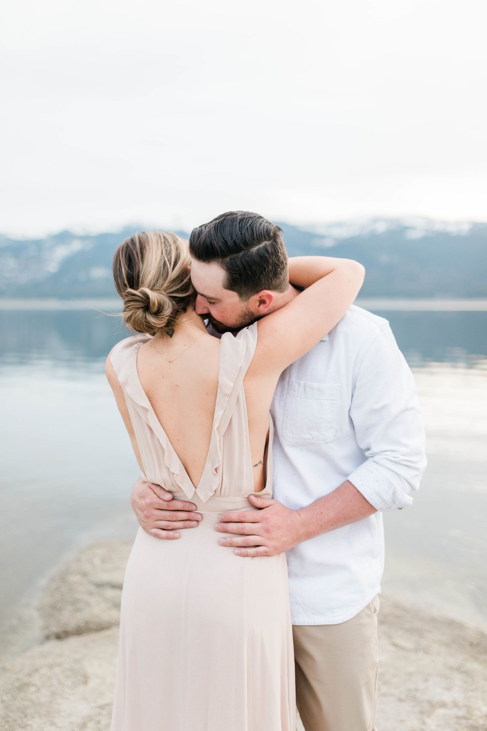 woman in a light pink gown with a low back embracing her fiance at their Idaho lake engagement photos