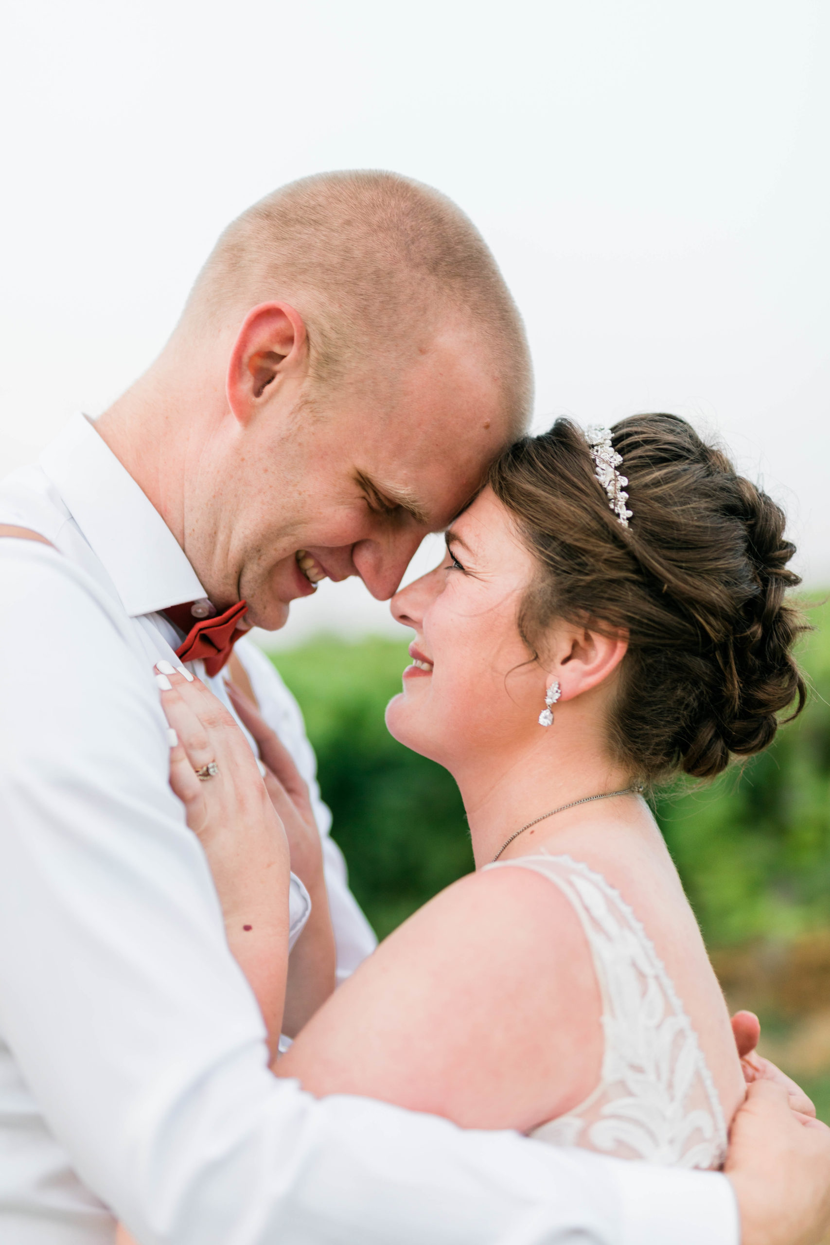 bride and groom embracing each other at their outdoor vineyard wedding with their heads together and smiling