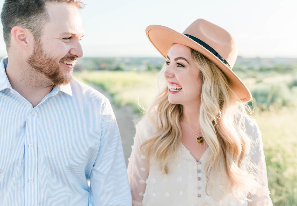 man in a blue button down and woman in a white blouse and hat holding hands and smiling together for their Idaho engagement session