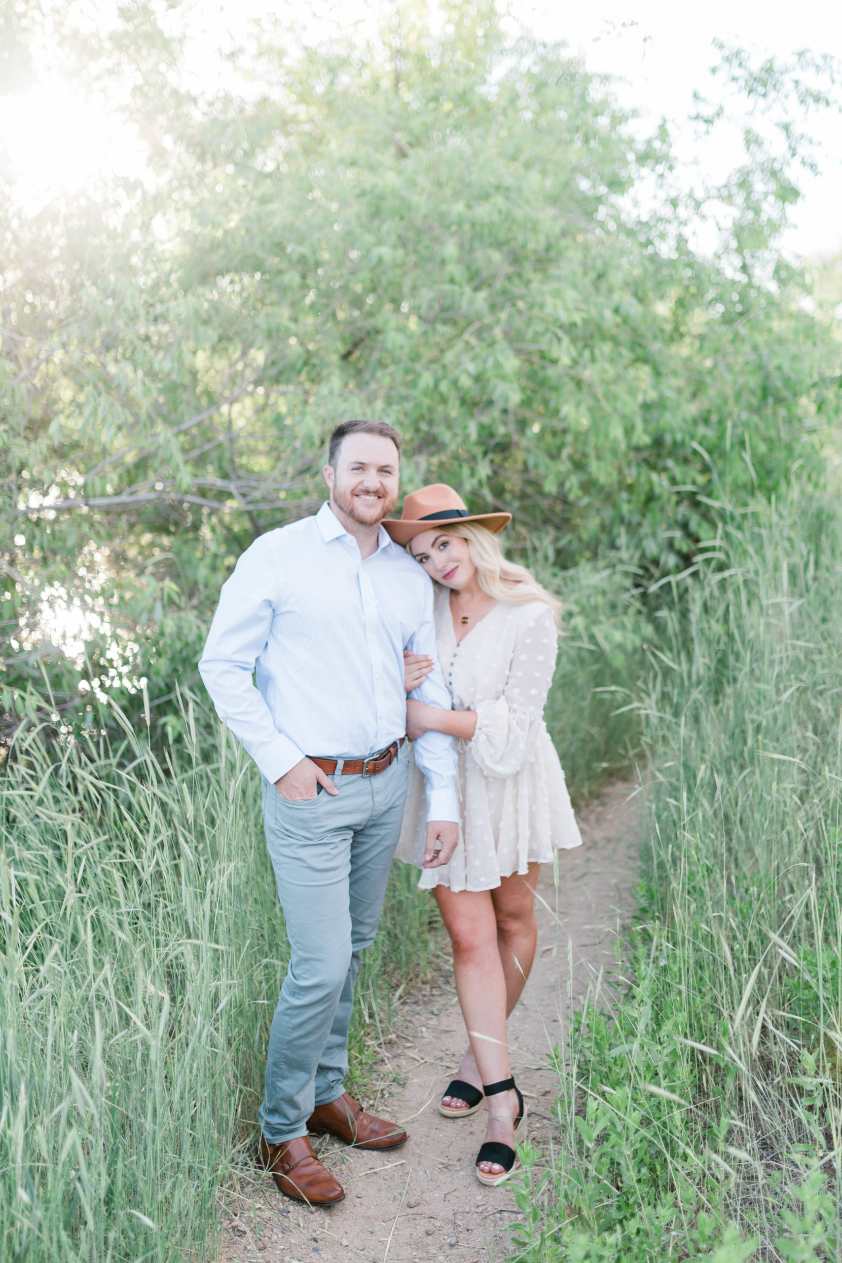 man and woman holding hands and leaning into each other for their Boise engagement photos with woman wearing a white dress and little hat