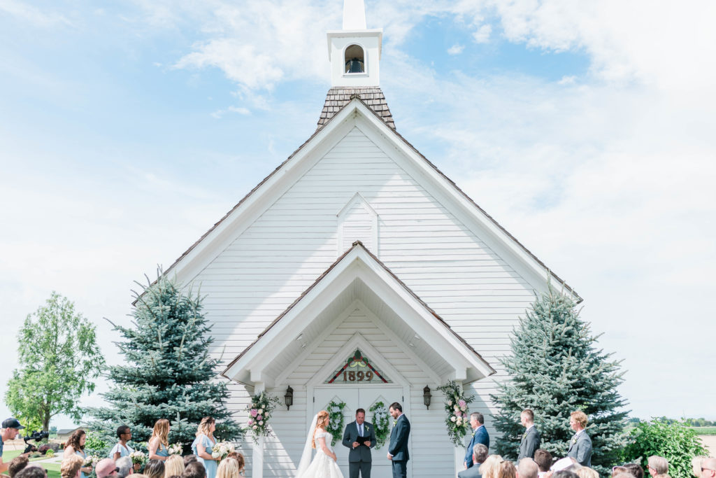 outdoor wedding ceremony in front of a white chapel with bride and groom saying their vows with their officiant