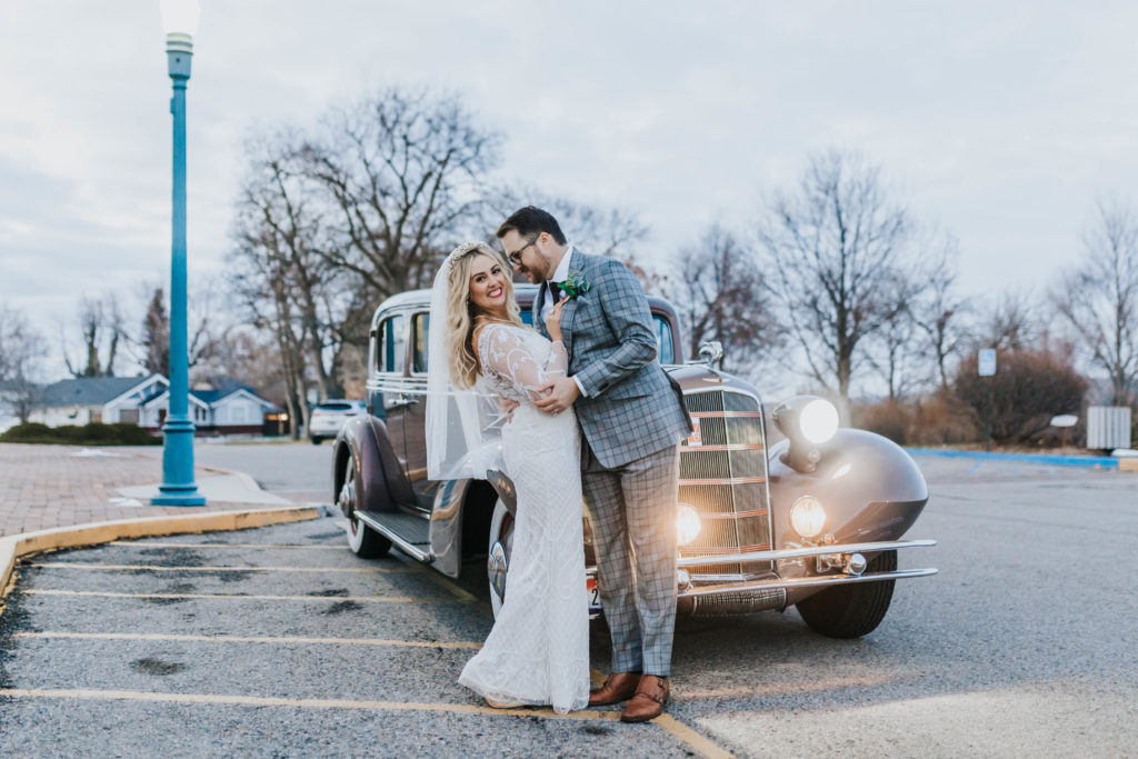 bride and groom kissing in front of their get away car for their wedding reception 