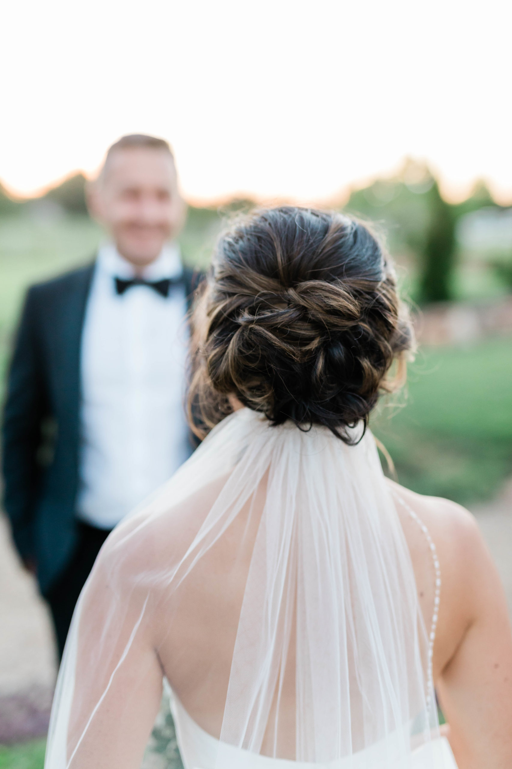 wedding updo for bride with a veil under the low bun as the bride walks to her groom