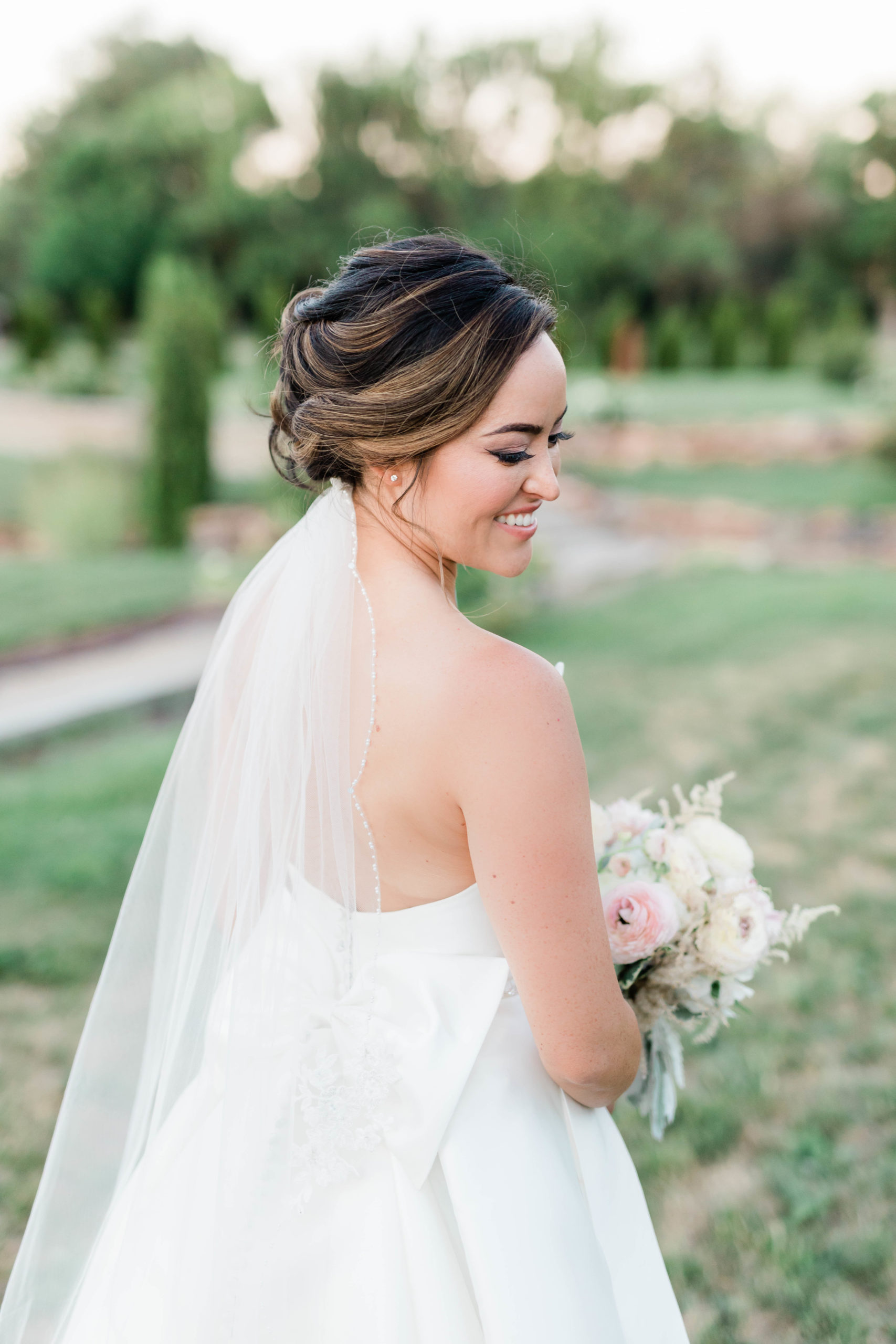 bride with dark brown hair and soft carmel highlights has a low bun with her veil underneath 