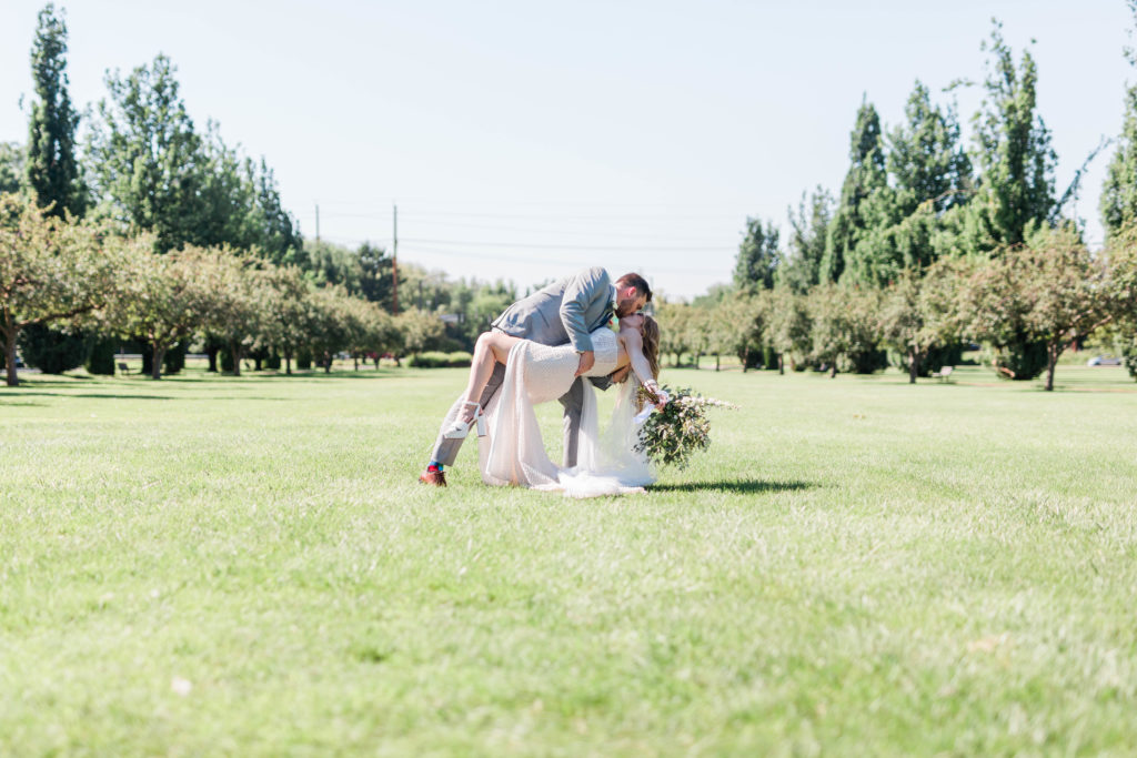 bride and groom dancing outside of their Boise wedding venue and the groom dips the bride back in a field 