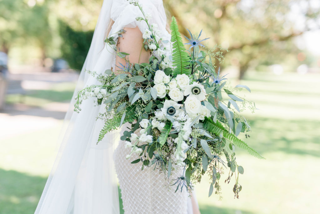 bride holding her white and light blue wedding bouquet as she walks in a field in Boise Idaho