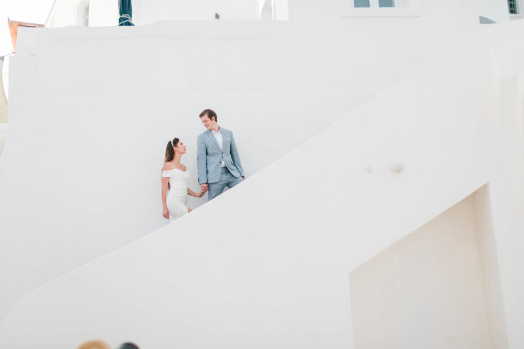 bride and groom holding hands and walking up a staircase together with white walls