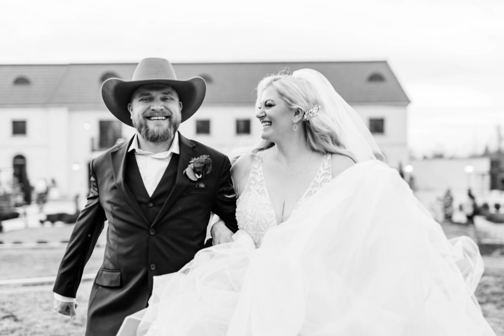 black and white wedding portrait of man smiling at the camera and his bride smiling at him as they run together 