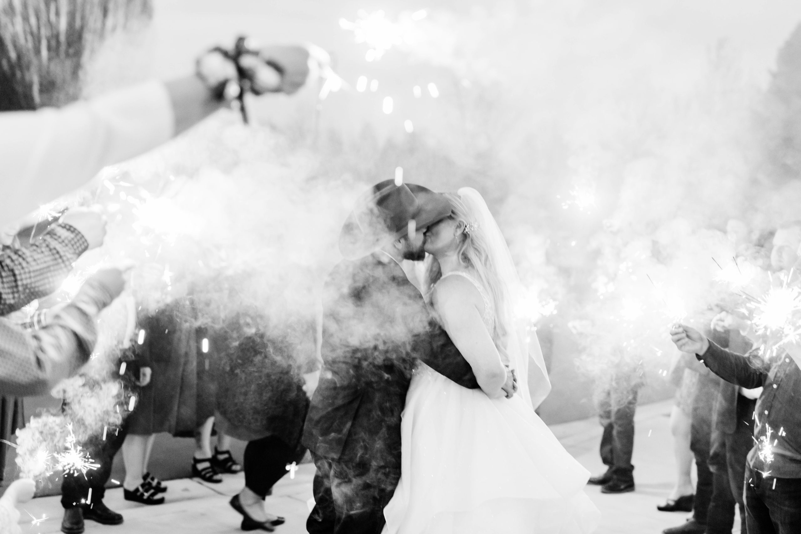 black and white wedding pictures of bride and groom kissing surrounding by smoke from their wedding exit sparklers