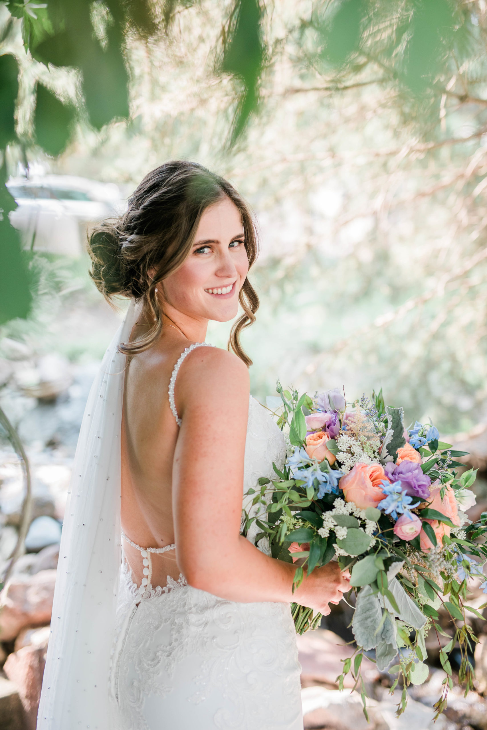 bride in a garden at her Boise wedding venue holding her colorful wedding bouquet while looking over her shoulder 