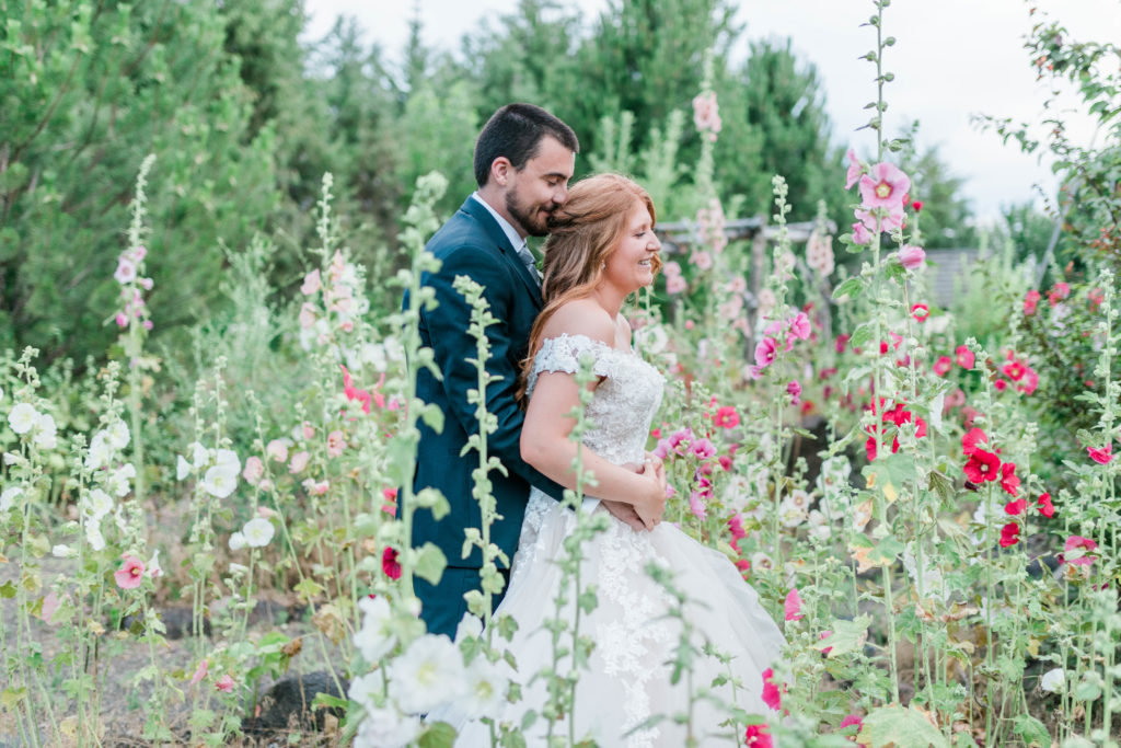 bride and groom standing in a dreamy wildflower field as the groom stands behind his bride and holds her waist