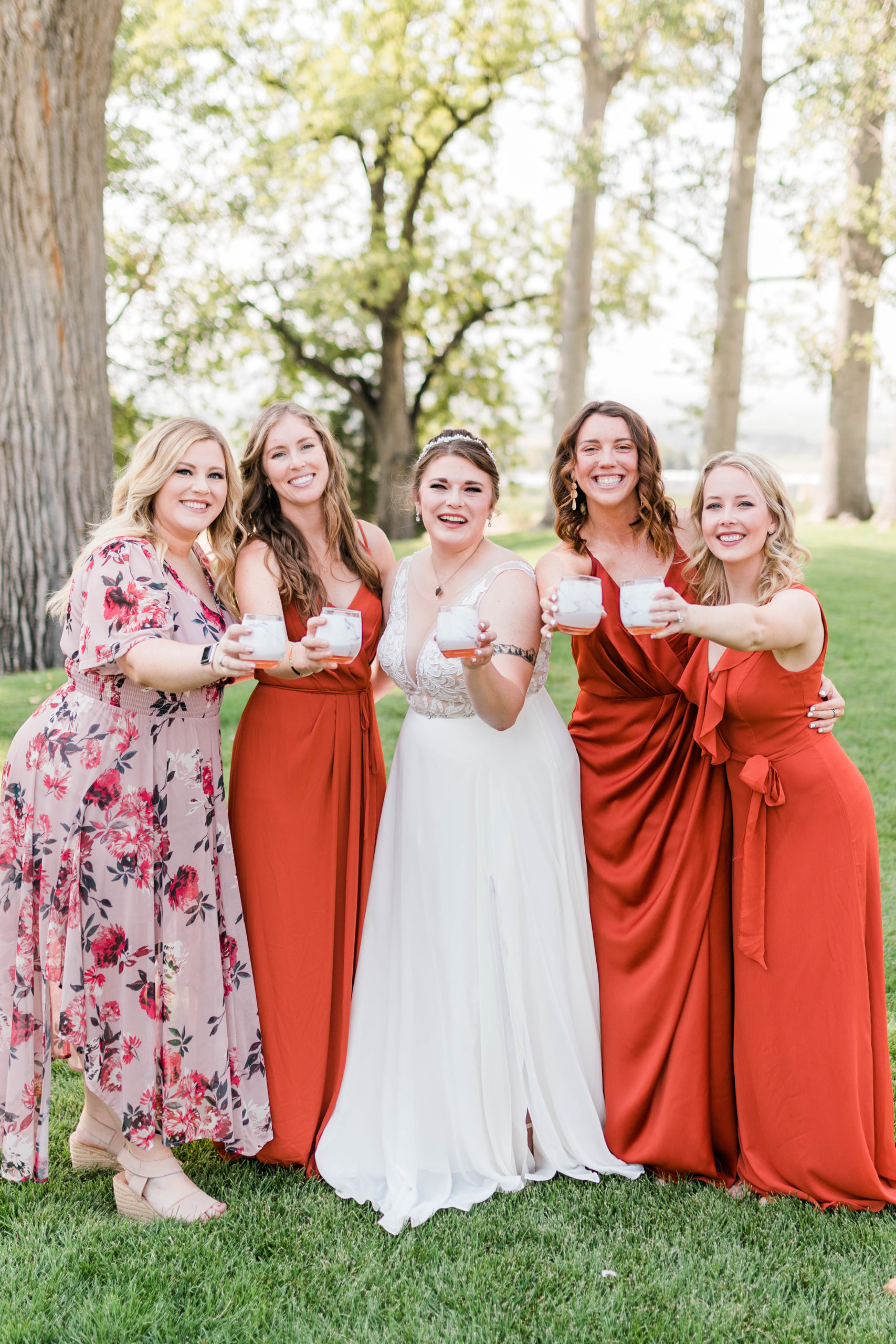 bride with her bridesmaids who are wearing a bright orange dress toasting their champagne together