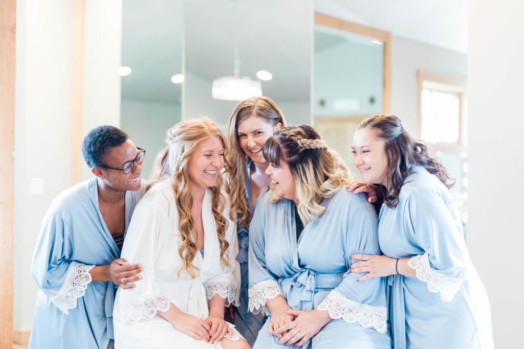 bride in a white robe surrounded by her bridesmaids in blue robs as they get ready at Still Water Hollow wedding venue in Nampa Idaho