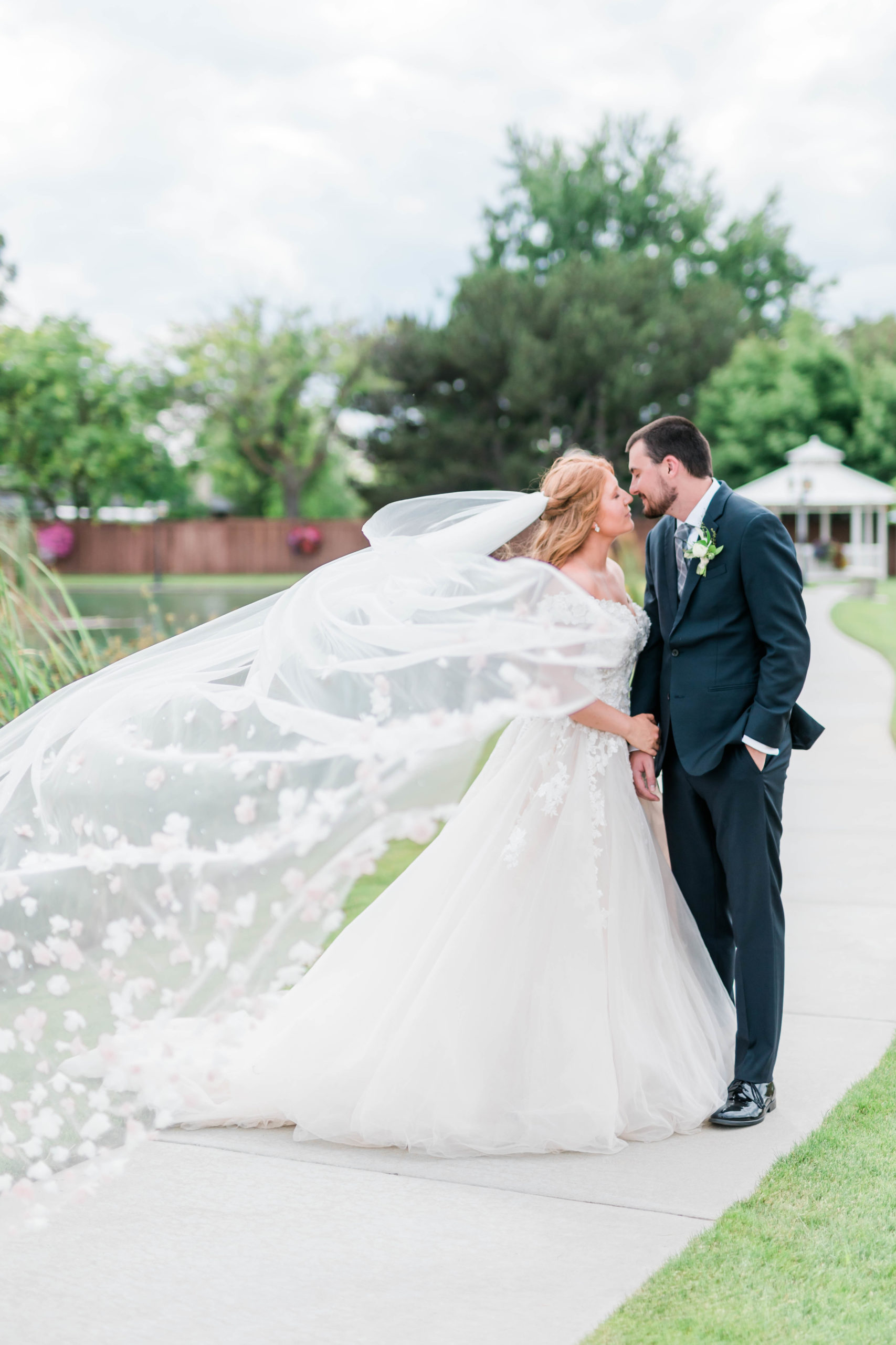 Boise wedding photographer captures bride adn groom holding hands as they lean into kiss each other and the brides veil blows in the wind