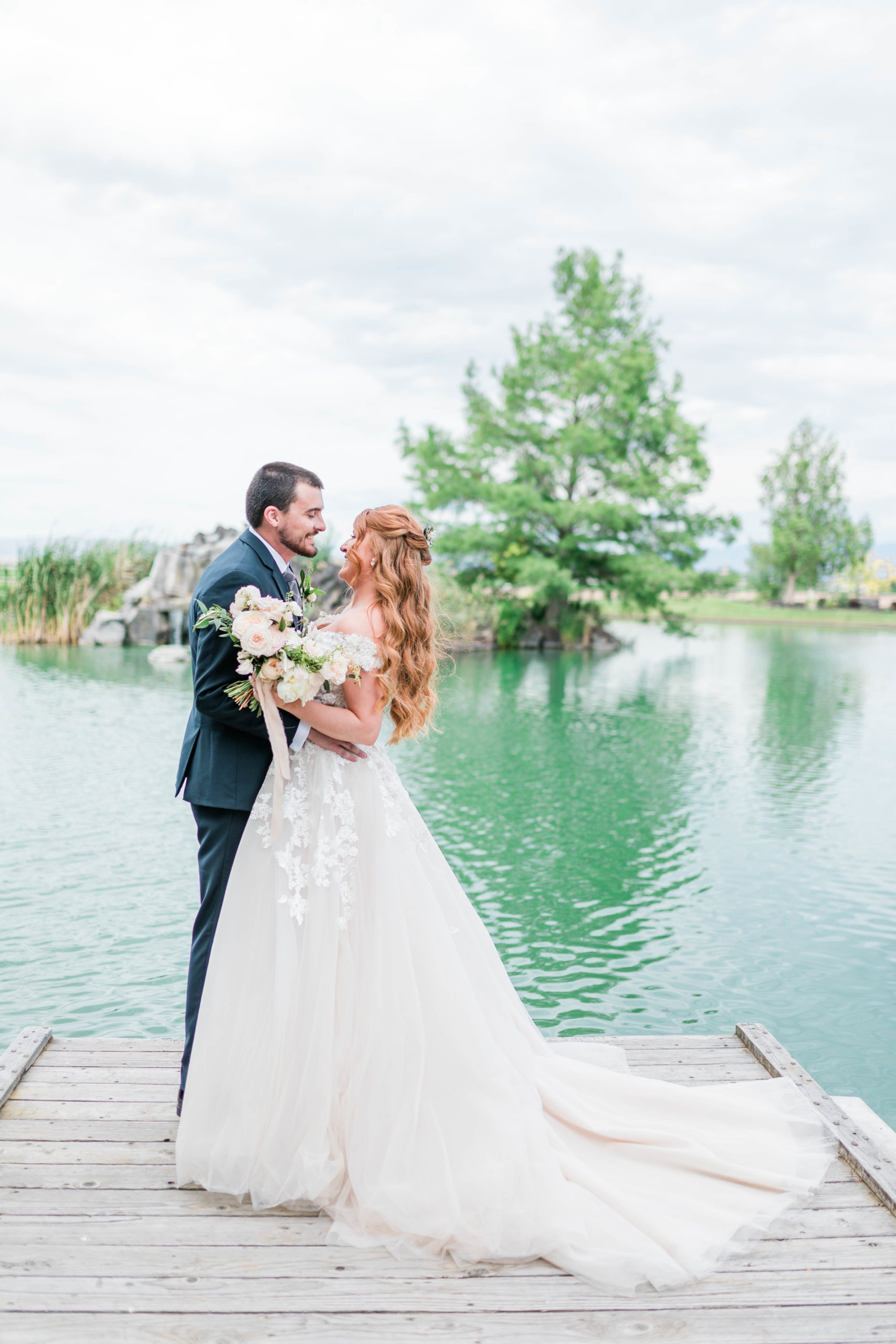 bride and groom standing on a pier on a lake as they embrace each other
