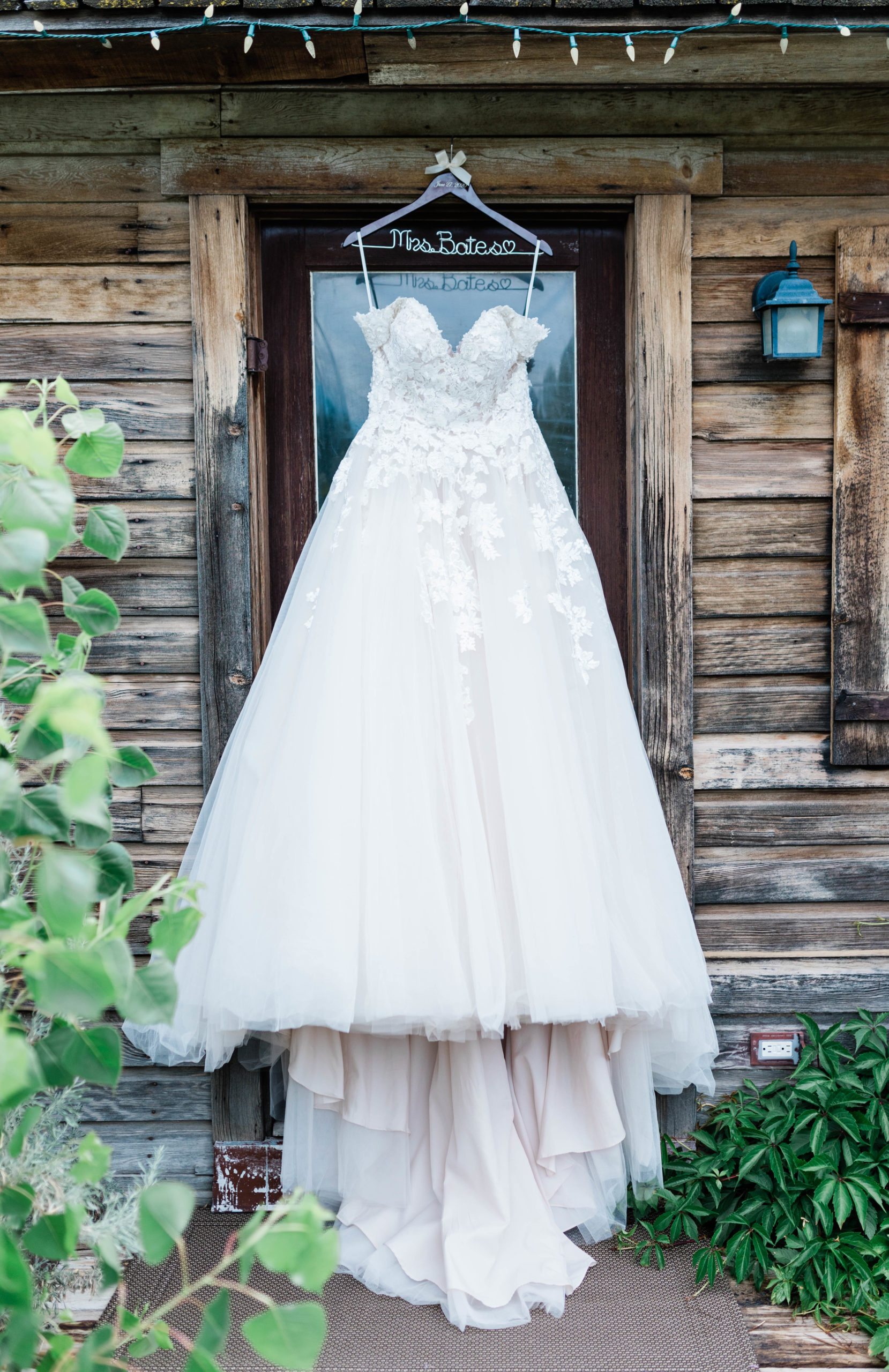 full lace and tulle wedding dress with floral detailing hanging from a wood hanger outside of Boise wedding venue