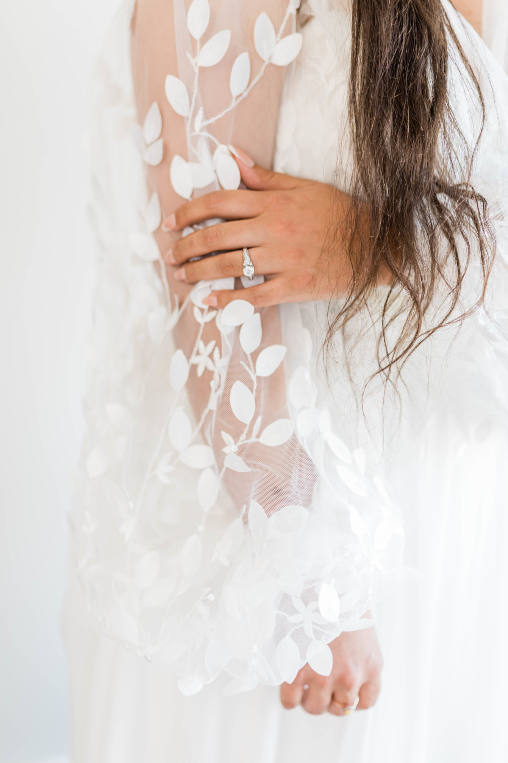 detail shot of brides engagement and wedding ring as she holds her dresses sleeve