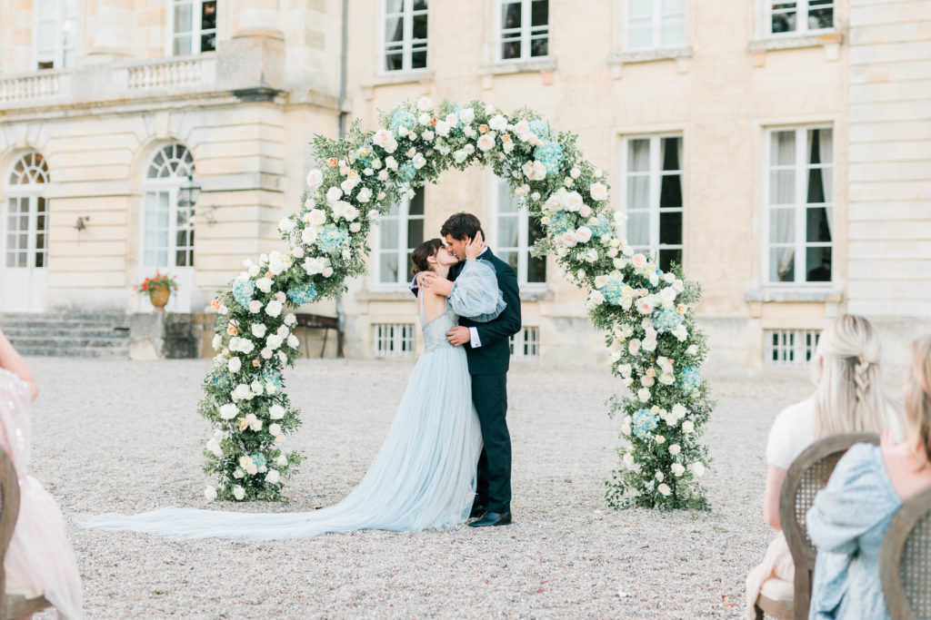 bride and groom kissing under arch at outdoor chateau de courtomer wedding ceremony