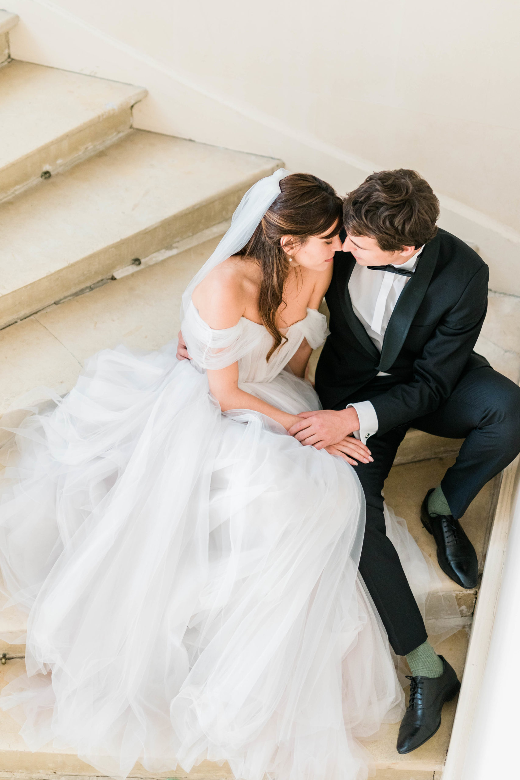 bride and groom sitting on the stairs of their Boise wedding venue while holding hands and leaning into each other taken by Boise Wedding Photographer