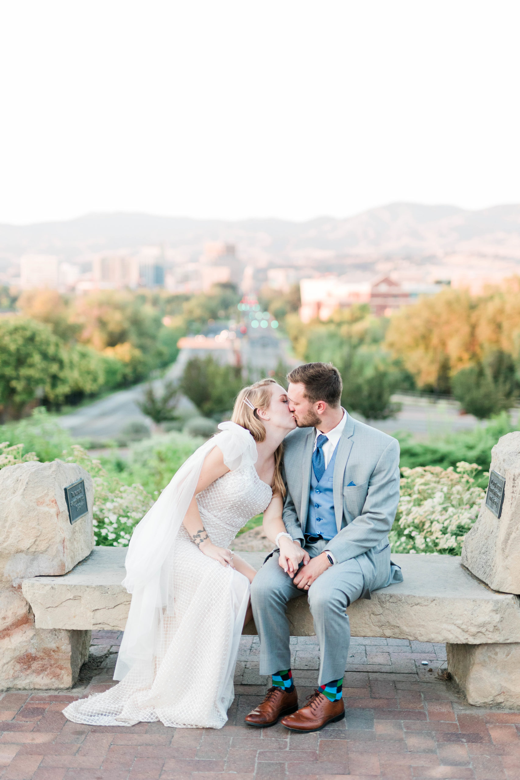 bride and groom kissing while sitting on a bench on top of a hill in Boise