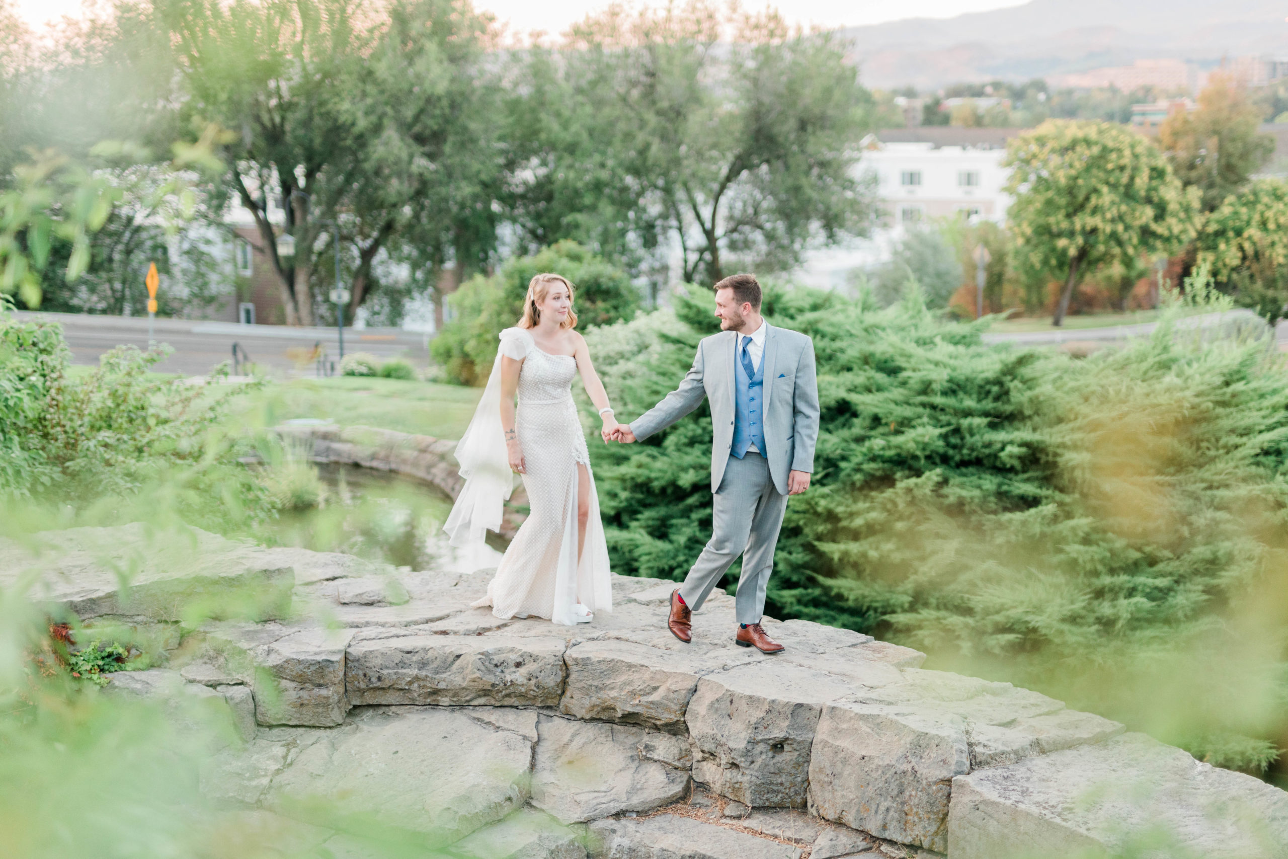 bride and groom holding hands and walking on a brick wall in a garden for their Boise wedding