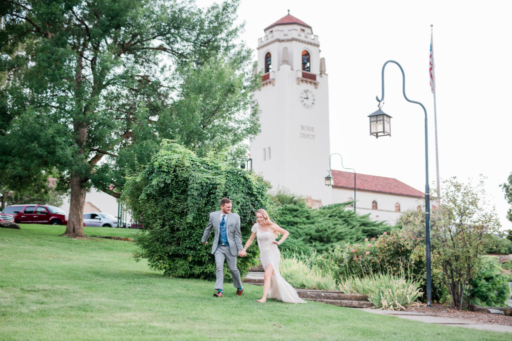 bride and groom holding hands and running through the lawn of the Boise Train Depot 