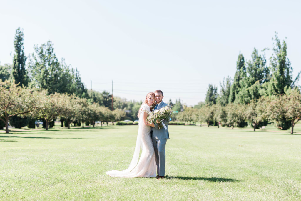 outdoor bridal photos at Boise Train Depot with bride and groom standing in a field together and leaning into one another and smiling 